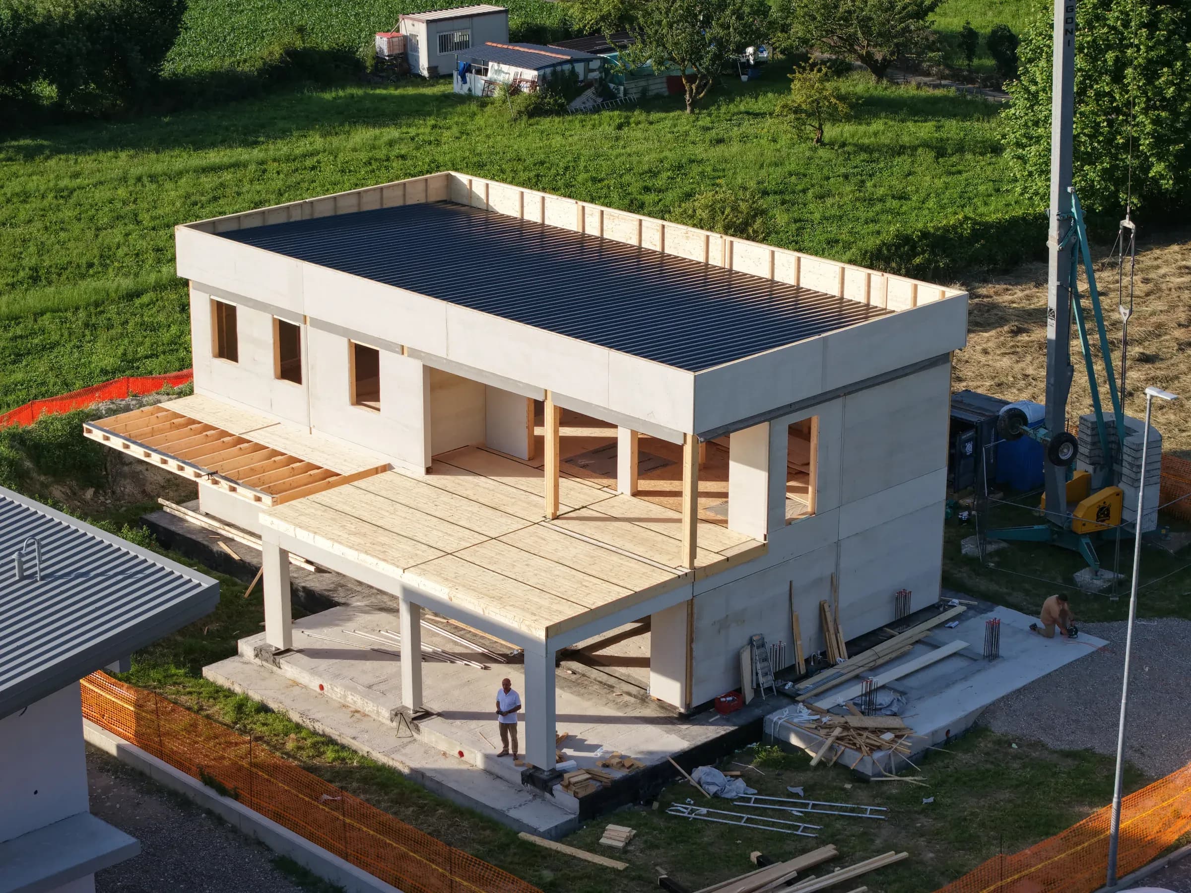 Residenza X-Frame a Brescia: struttura in fase di montaggio con copertura piana e terrazza su pilotis, sullo sfondo le Prealpi